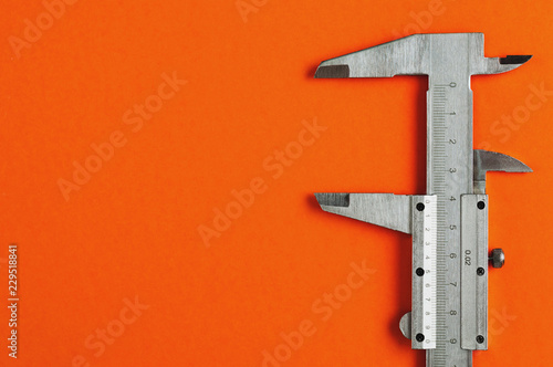 Vernier caliper of gray color on orange table with copy space for your text photo