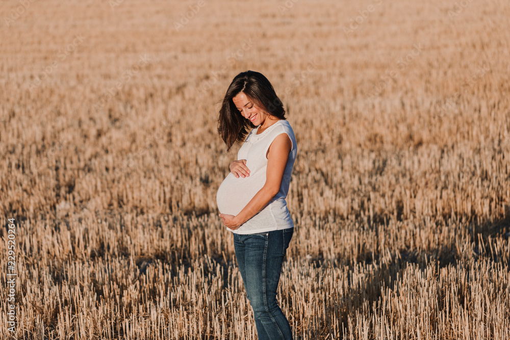 portrait outdoors of a young beautiful pregnant woman touching her belly while expecting a baby. Outdoors lifestyle. Yellow background portrait outdoors of a young beautiful pregnant woman touching her belly while expecting a baby. Outdoors lifestyle. Yellow background