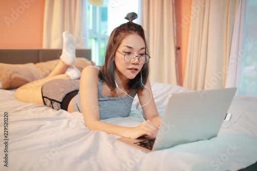 beautiful and sexy woman using laptop computer and listening to music from cell phone on bed