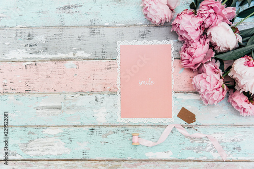 Fototapeta Naklejka Na Ścianę i Meble -  pink peony flowers with greeting card on wooden background. Minimal flat lay composition with copy space.