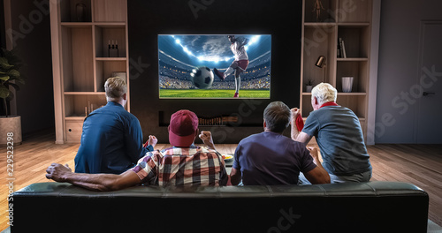 Group of fans are watching a soccer moment on the TV and celebrating a goal, sitting on the couch in the living room. photo