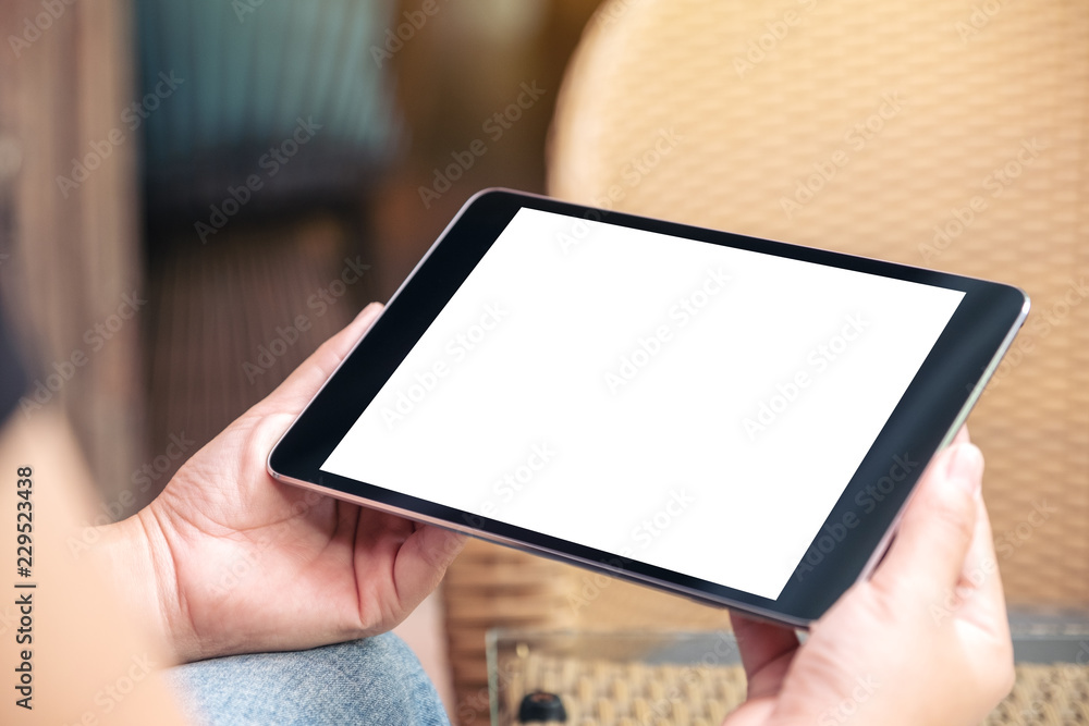 Mockup image of a woman sitting and holding black tablet pc with blank white desktop screen