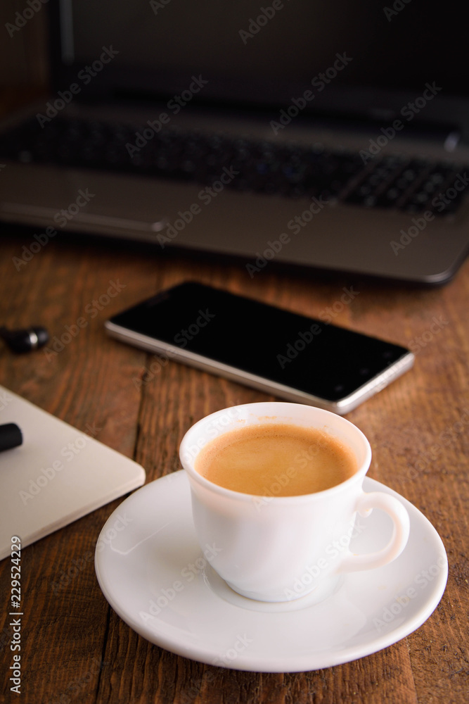 Cup of coffee on a laptop keyboard. Work place modern. Laptop (notebook) with cup of coffee and notepad with pen on old wooden table. Cup of coffee on a laptop keyboard. Work place modern. Laptop (notebook) with cup of coffee and notepad with pen on old wooden table.