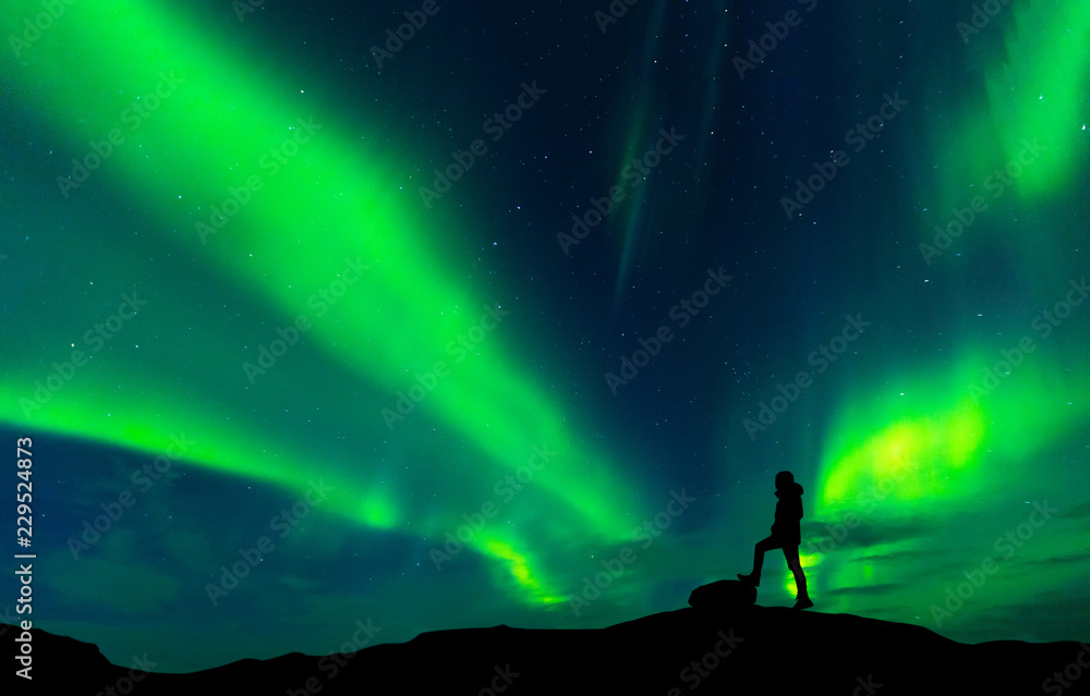 Fototapeta premium Aurora borealis with silhouette standing man on the mountain.Freedom traveller journey concept