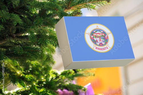 Minnesota state flag printed on a Christmas gift box. Printed present box decorations on a Xmas tree branch on a street. Christmas shopping in United States, local market sale and deals concept. photo