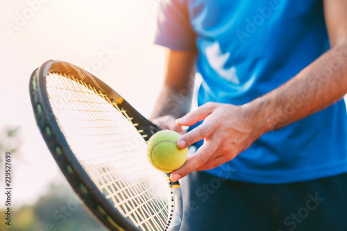 Guy holding tennis racket and ball on clay court. Boy getting ready for a serve in tennis. © kojala