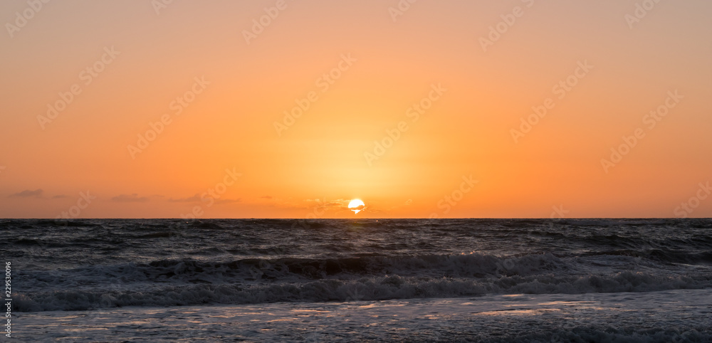 Photo of centered position sunrise at a beach with an orange and pink sky.