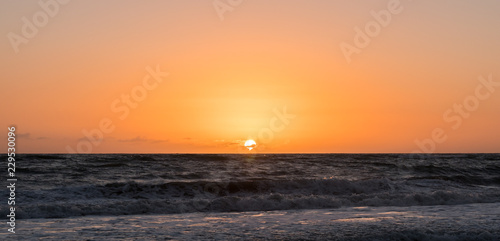Photo of centered position sunrise at a beach with an orange and pink sky.