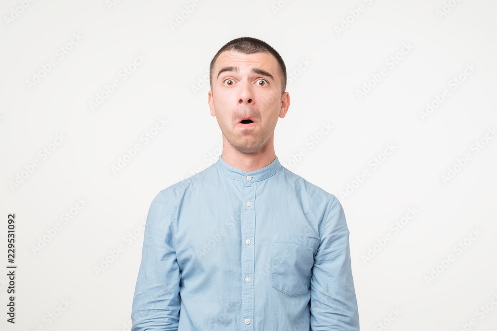 Portrait of fearful young man in blue shirt keeping mouth wide open, feeling stressed Portrait of fearful young man in blue shirt keeping mouth wide open, feeling stressed
