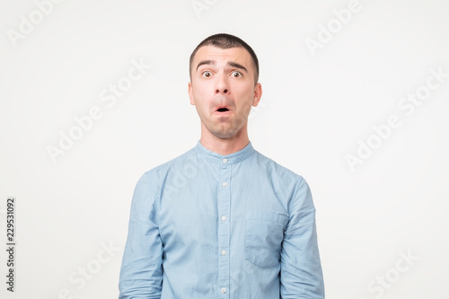 Portrait of fearful young man in blue shirt keeping mouth wide open, feeling stressed