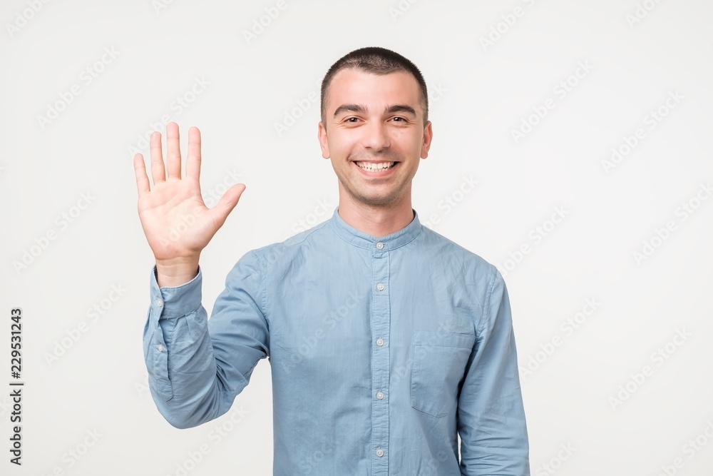 Attractive european student waives hand in hello gesture while smiling cheerfully over white background. Attractive european student waives hand in hello gesture while smiling cheerfully over white background.