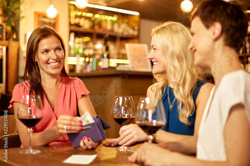 leisure  payment and lifestyle concept - happy women with money in wallet paying bill at restaurant or wine bar