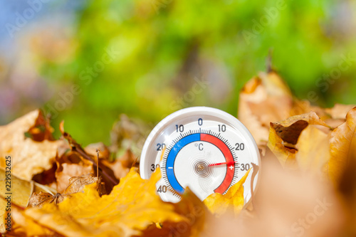 Outdoor thermometer in golden maple leaves shows warm temperature - hot indian summer concept photo