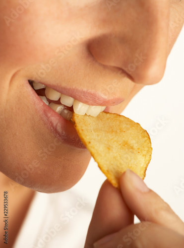 YOUNG WOMAN EATING SINGLE POTATO CRISP IN CLOSE UP