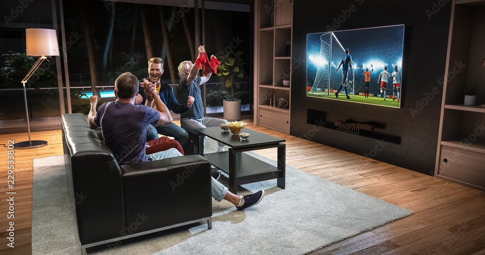 Group of fans are watching a soccer moment on the TV and celebrating a goal, sitting on the couch in the living room. Group of fans are watching a soccer moment on the TV and celebrating a goal, sitting on the couch in the living room.