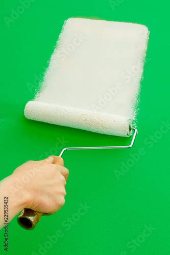 ROLLER APPLYING WHITE PAINT TO GREEN WALL