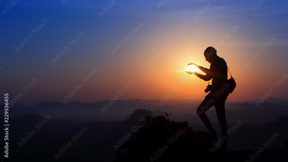 Silhouette of man holding sun on the mountain
