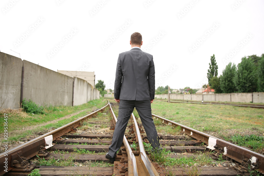 Businessman standing on railway tracks. Concept of choice