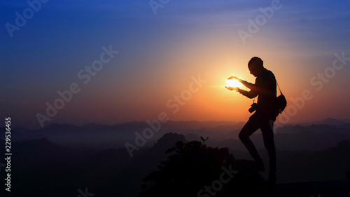 Silhouette of man holding sun on the mountain © Nandhu