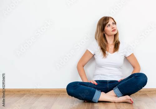 dreaming woman with long hair wearing casual clothes sit on a floor on white background with copy space