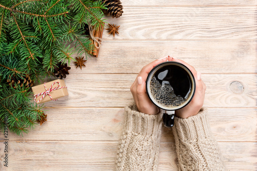 female hands holding coffee cupon wooden table with chrisstmas decoration. Top view with copy space photo