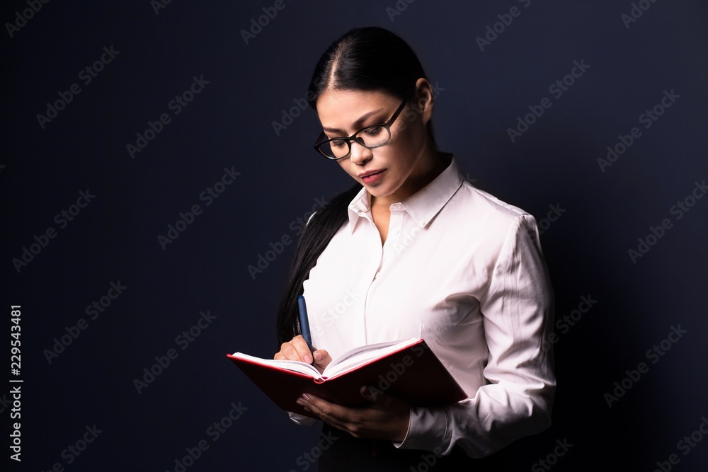 Thoughtful business woman in glasses making notes. Isolated on dark background. Thoughtful business woman in glasses making notes. Isolated on dark background.