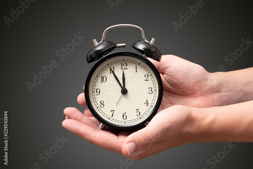 Hand holding clock with five minutes to twelve o'clock photo