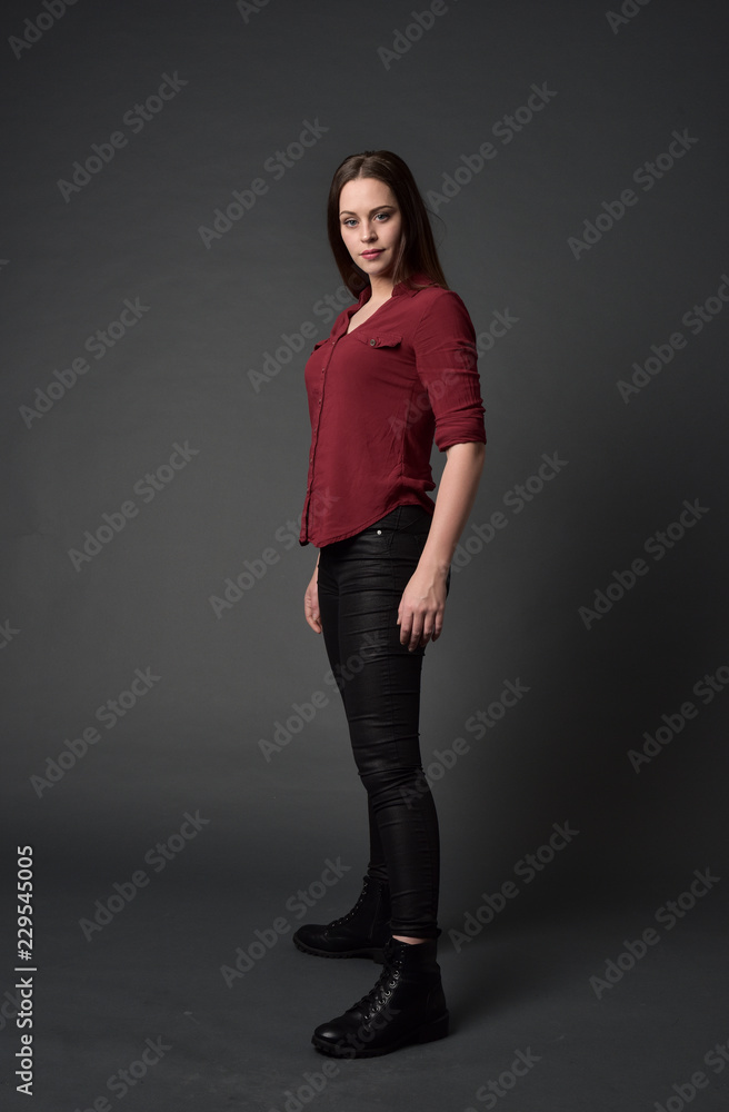 full length portrait of brunette girl wearing red shirt and leather pants. standing pose, on grey studio background. full length portrait of brunette girl wearing red shirt and leather pants. standing pose, on grey studio background.