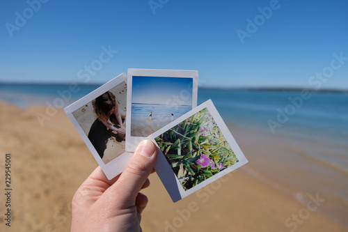 Hand holding instant photos taken at the beach