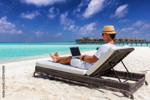 Arbeit im Urlaub: Geschäftsmann mit Laptop auf Liege am tropischen Strand photo