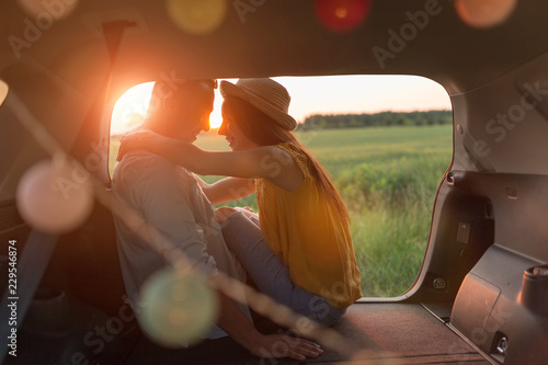 Young couple sitting in their car trunk and watching the sunset