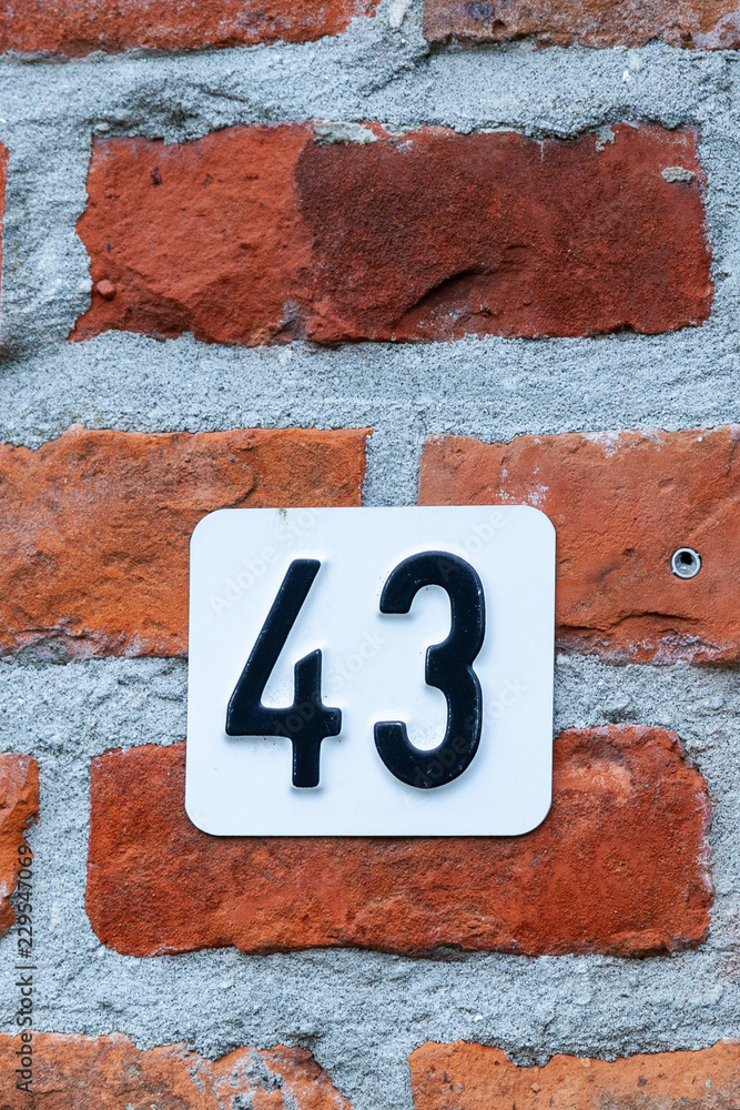 New house number forty-three 43 in pressed metal black digits on white background and attached to red house bricks from Belgium New house number forty-three 43 in pressed metal black digits on white background and attached to red house bricks from Belgium