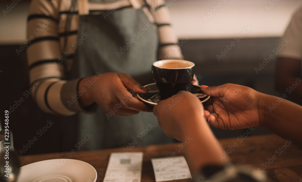 Closeup of an African barista giving a customer her cappuccino