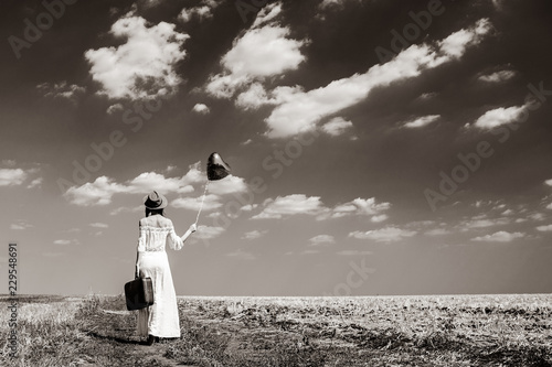 photo of the beautiful young woman with heart-shaped balloon and suitcase in the field