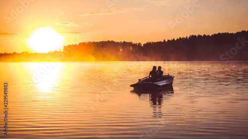 Couple in love ride in a rowing boat on the lake during sunset. Romantic sunset in golden hour. Happy woman and man together relaxing on water nature around
