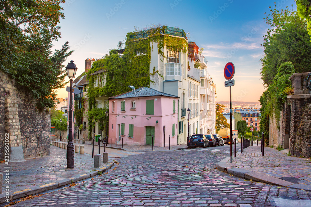 Naklejka premium Przytulna stara ulica z różowym domem przy słonecznym wschodzie słońca, ćwiartka Montmartre w Paryż, Francja