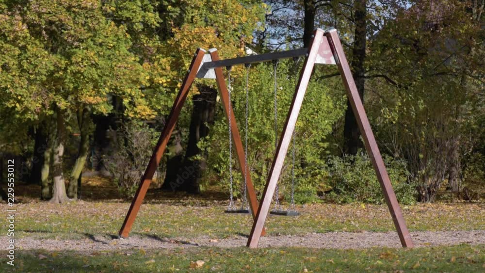 Abandoned empty swings swaying in the wind at children playground outdoors - in a park an autumn sunny day. Abandoned empty swings swaying in the wind at children playground outdoors - in a park an autumn sunny day.