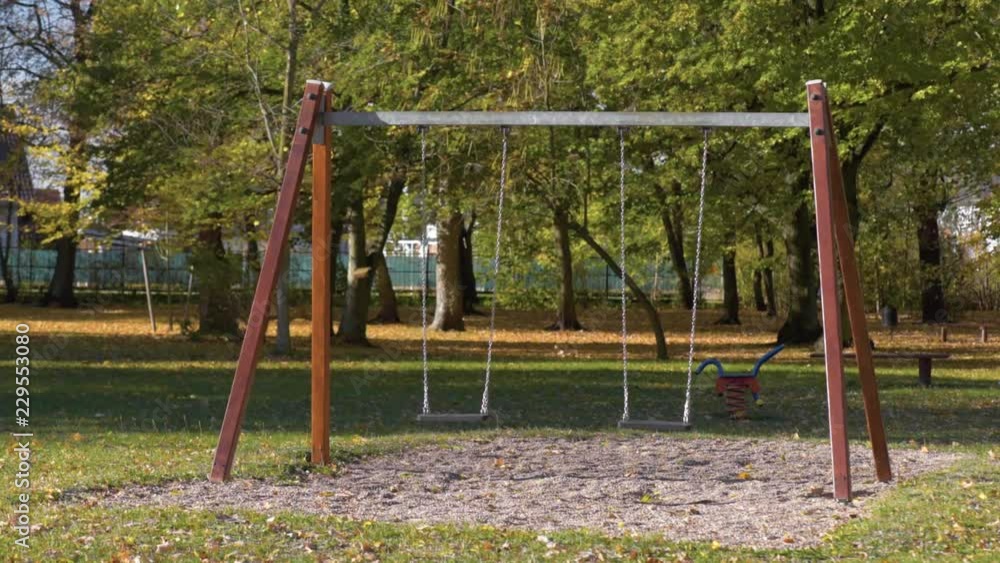 Abandoned empty swings swaying in the wind at children playground outdoors - in a park an autumn sunny day. Abandoned empty swings swaying in the wind at children playground outdoors - in a park an autumn sunny day.