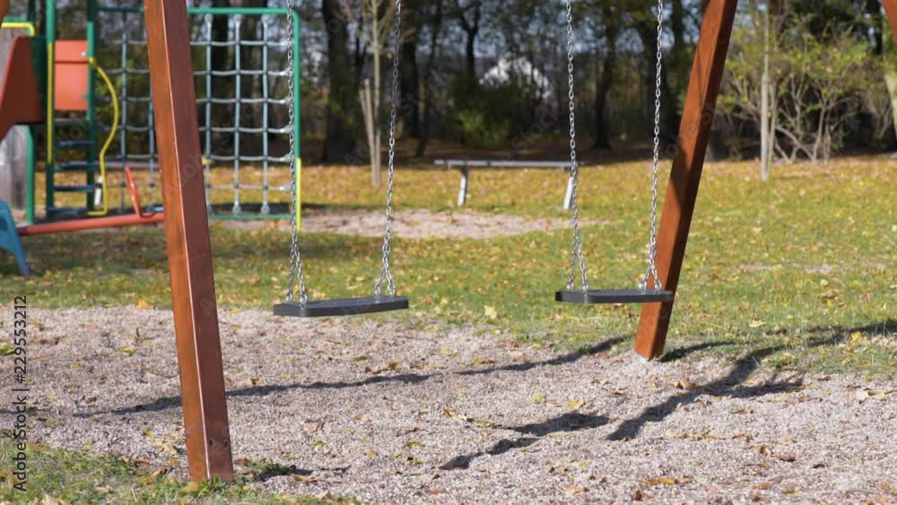 Abandoned empty swings swaying in the wind at children playground outdoors - in a park an autumn sunny day. Abandoned empty swings swaying in the wind at children playground outdoors - in a park an autumn sunny day.