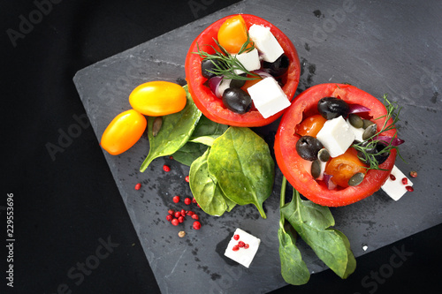 Pomidory nadziewane. Pomidory faszerowane oliwkami, serem feta, szpinakiem podane na czarnym talerzu.