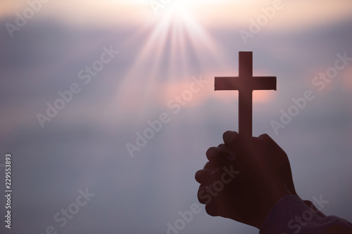 Silhouette of teen girl hands holding wooden cross on sunrise background, Crucifix, Symbol of Faith.