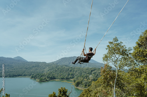 young asian man swinging from high top hill