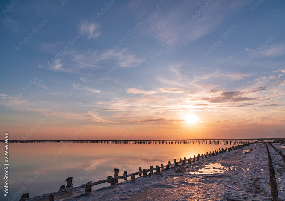 sunset on a pink salt lake, a former mine for the extraction of pink salt. row of wooden pegs overgrown with salt