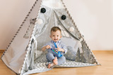 Cute one year old baby playing in a tent, wigwam. Shadow depth of field, natural light. The interior of the children's room is grey, blue and white