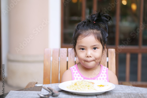 Asian child or kid girl enjoy eating spaghetti with egg delicious food on wood table with smile and happy for morning breakfast or lunch in restaurant or nursery preschool and kindergarten food court