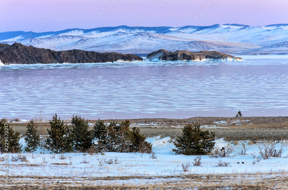Landscape with beautiful winter frozen lake and snowy mountains at sunset at lake Baikal. Panoramic view