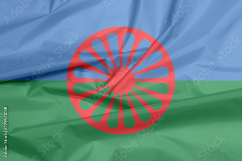 Fabric flag of Romani people. Crease of the Gypsies flag background, blue and green background, representing the heavens and earth and red chakra or cartwheel in the center.