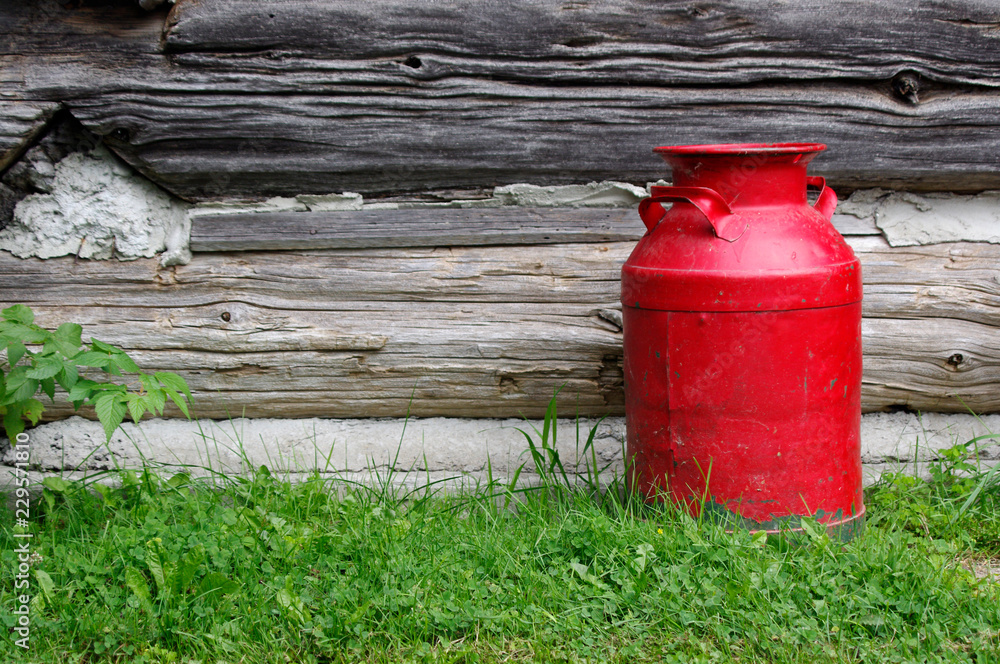 Old fashioned red milk can by log cabin wall background Old fashioned red milk can by log cabin wall background