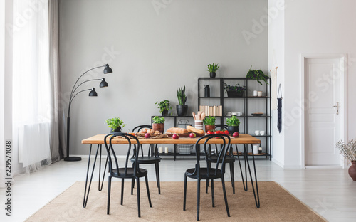 Black chairs at wooden table with food in grey dining room interior with plants and lamp. Real photo