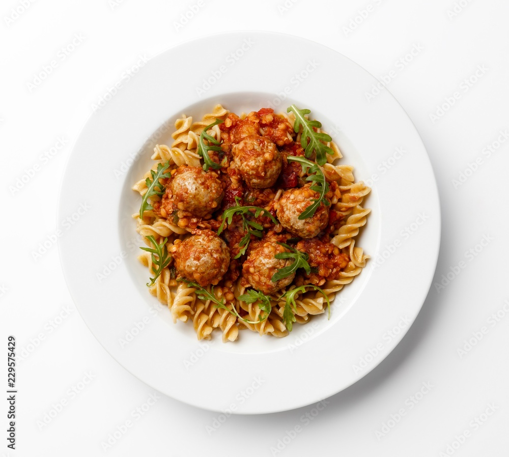 Fototapeta premium Meatballs in a tomato sause with paste twists with a rocket garnish, on a white plate.